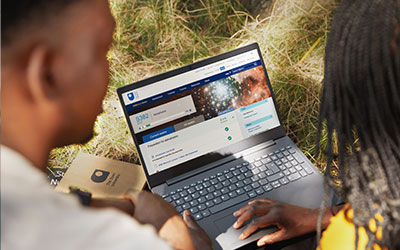 People looking at an OU course on a laptop, outside on a sunny day