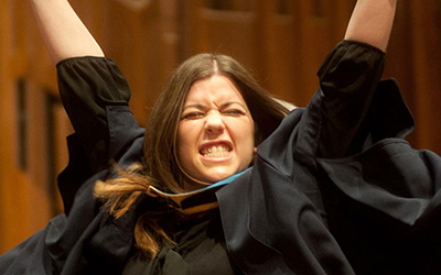 A graduate celebrating with arms raised