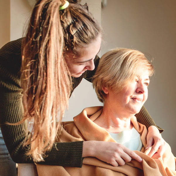 A young carer wrapping a blanket around a seated individual